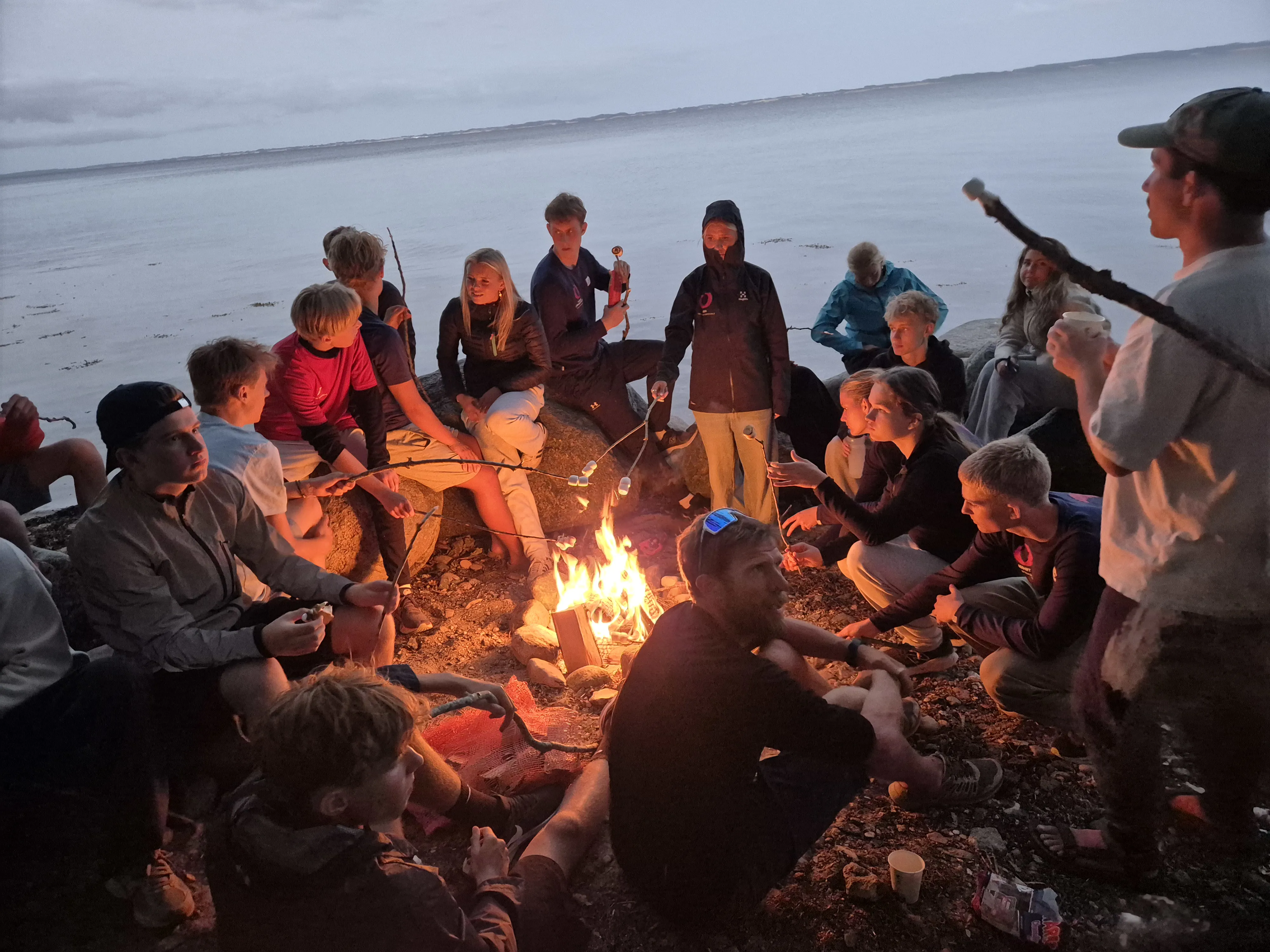 Efterskoleelever der sidder rundt om et bål i strandkanten på sydfyn