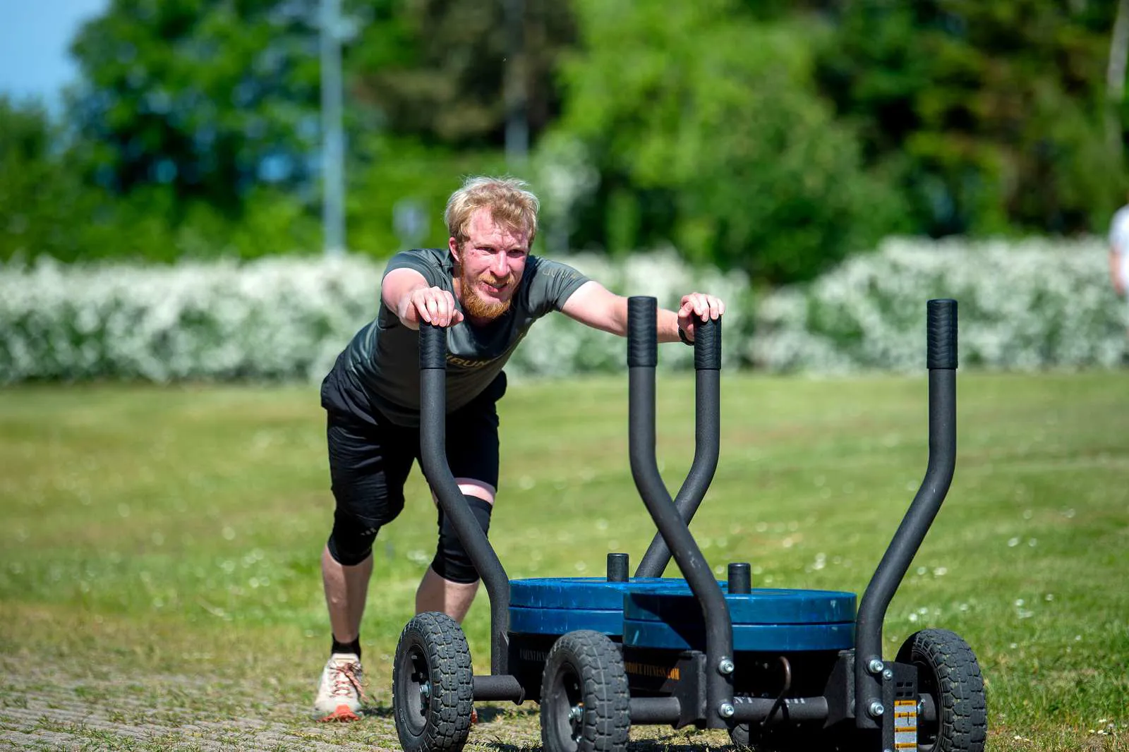 En højskoleelev, der dyrker Hyrox udendørs og skubber noget tungt