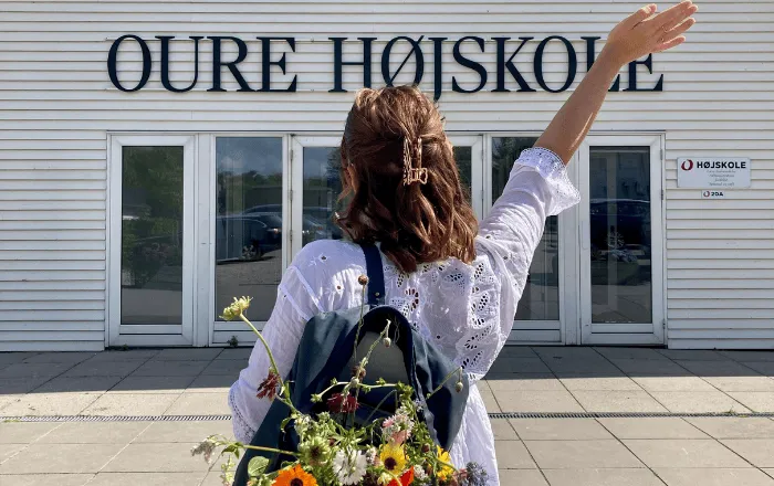 Pige foran Oure Idrætshøjskole med blomster i tasken